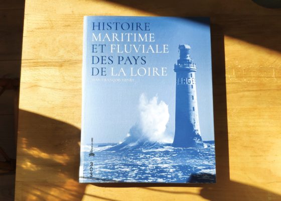 Photographe : Eloïse Bugeau. Coédition : 303 et Région Pays de la Loire. Auteur : Jean-François Henry. Couverture du livre "Histoire maritime et fluviale des Pays de la Loire" représentant une vague s'écrasant sur un phare en pleine mer.