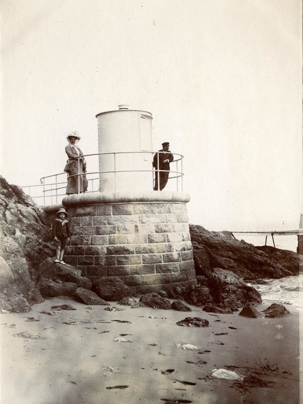 Photographie représentant un homme, une femme et un enfant qui posent devant l'ancien feu antérieur de Porcé, anse de la Belle-Fontaine.