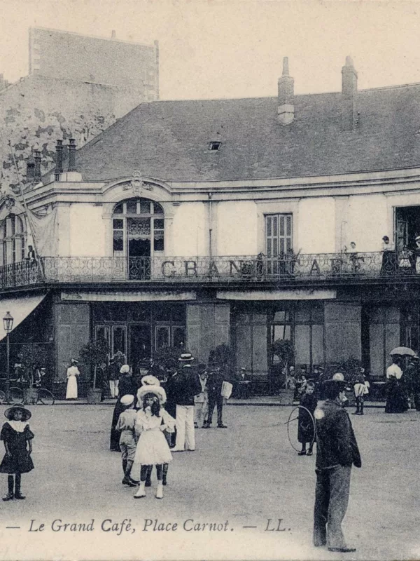 Photographe : inconnu. Éditeur : L.L. Collection Saint-Nazaire Agglomération Tourisme – Écomusée. Carte postale avec une photo en noir et blanc représentant une foule devant le Grand Café, place Carnot à Saint-Nazaire.