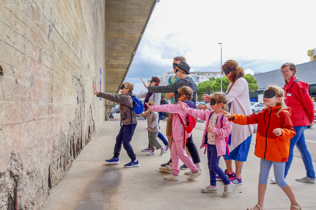 Enfants et adultes avec un bandeau sur les yeux s'avançant vers un mur en béton de la base.