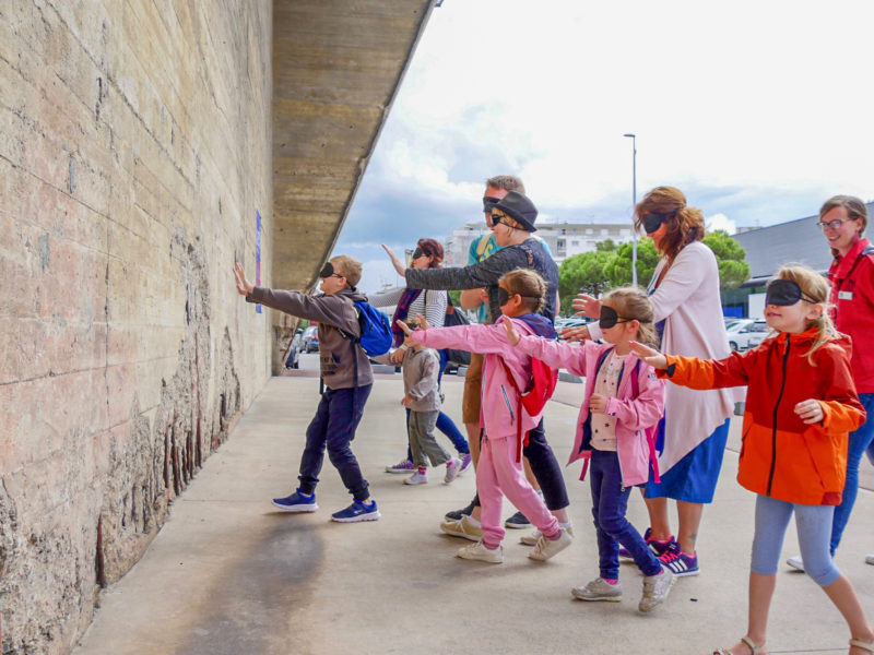 Enfants et adultes avec un bandeau sur les yeux s'avançant vers un mur en béton de la base.