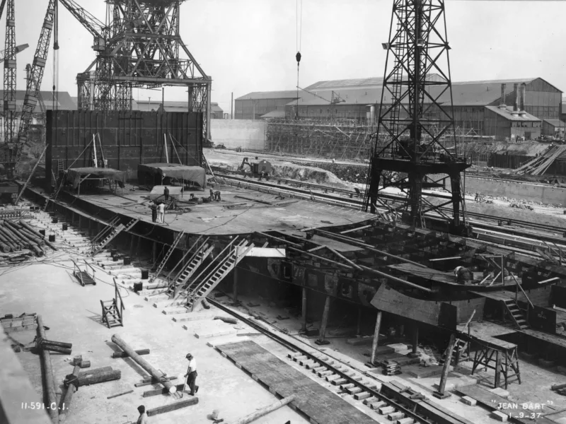 Photographe : Inconnu. Collection Saint-Nazaire Agglomération Tourisme – Écomusée. Fonds Chantiers de l’Atlantique. Montage de la coque du cuirassé Jean Bart le 1er septembre 1937.