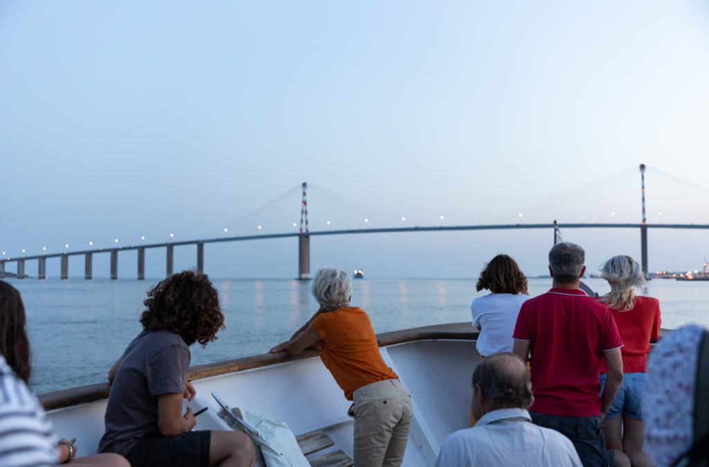 Passagers appuyés sur le pont du bateau de croisière et regardant le pont de Saint-Nazaire à la nuit tombée.