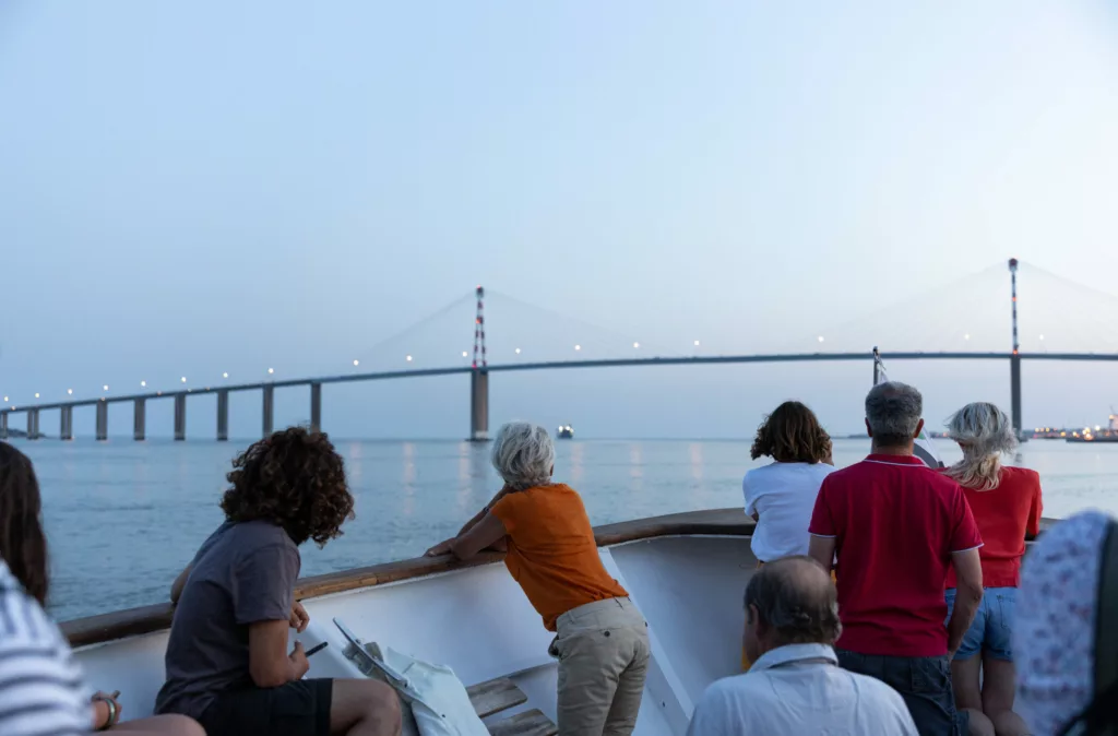 Photographe : Jean-Félix Fayolle. Département de Loire-Atlantique Passagers appuyés sur le pont du bateau de croisière et regardant le pont de Saint-Nazaire à la nuit tombée.
