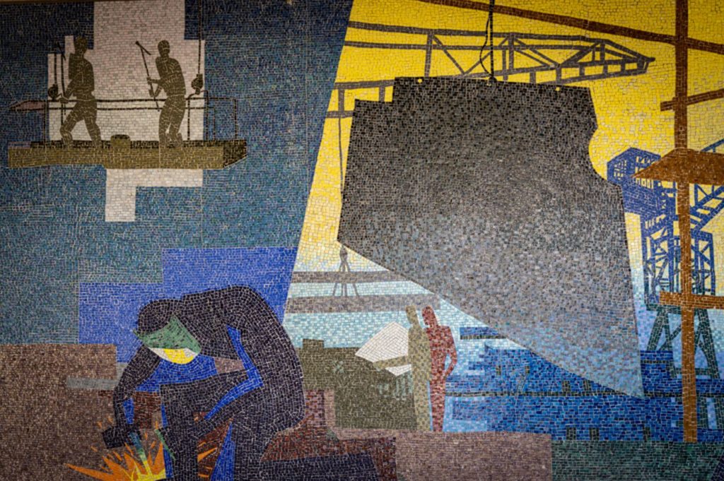 Photographie d'une mosaïque colorée représentant les chantiers navals et un soudeur au premier plan dans des tons colorés.