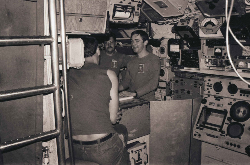 Photographie en noir et blanc de l'équipage dans le central opérations du sous-marin, pendant la Mission Thazard