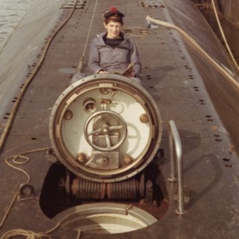 Sous-marinier en uniforme posant devant l'écoutille du sous-marin Espadon.