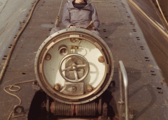 Sous-marinier en uniforme posant devant l'écoutille du sous-marin Espadon.
