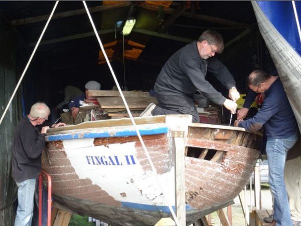 Quatre hommes s'affairent à la restauration d'un ancien navire.