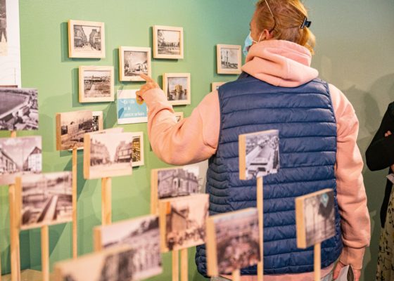 Femme montrant du doigt une carte postale encadrée au mur dans l'exposition "Regard miroir ou le paysage réinventé" à l'Écomusée de Saint-Nazaire