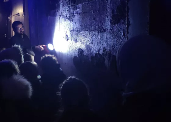 Guide lors d'une visite guidée éclairant un mur de la base sous-marine à la lampe torche pour montrer des graffitis.