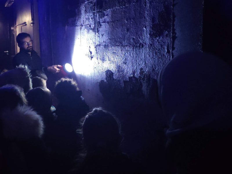 Photographe : Eloïse Bugeau. Saint-Nazaire Agglomération Tourisme Guide lors d'une visite guidée éclairant un mur de la base sous-marine à la lampe torche pour montrer des graffitis.