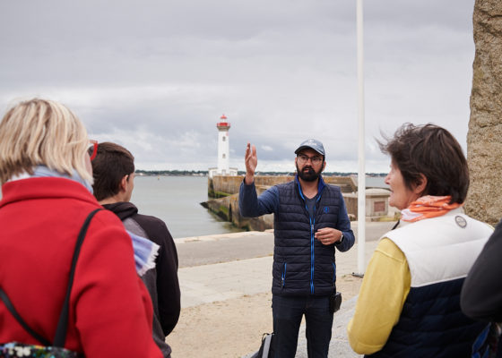 Photographe : Rudy Burbant. Guide et groupe de visiteurs en extérieur près du vieux môle lors d'une visite guidée sur l'opération Chariot.