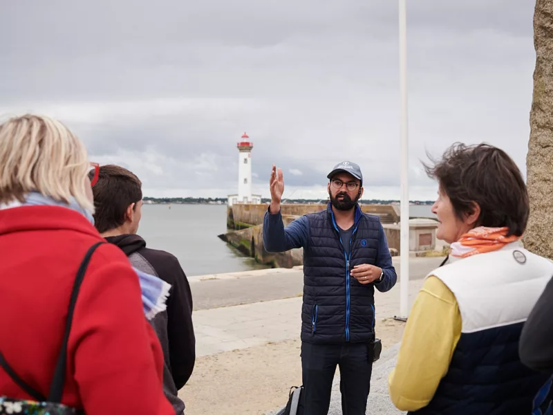 Photographe : Rudy Burbant. Guide et groupe de visiteurs en extérieur près du vieux môle lors d'une visite guidée sur l'opération Chariot.