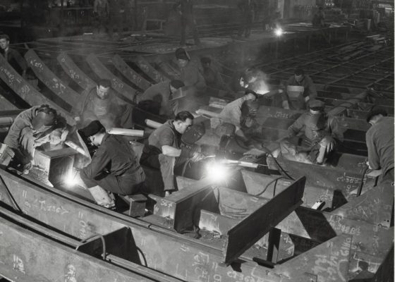 Photographie en noir et blanc représentant des soudeurs dans un atelier de préfabrication des Chantiers de l'Atlantique.