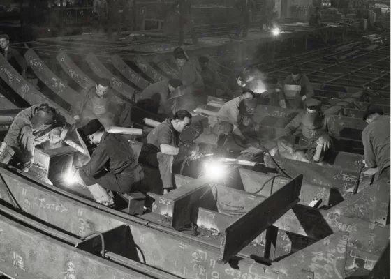 Photographie en noir et blanc représentant des soudeurs dans un atelier de préfabrication des Chantiers de l'Atlantique.