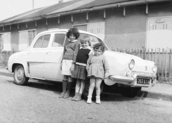 Photographie en noir et blanc d'enfants posant devant une voiture et un baraquement provisoire pendant la reconstruction de Saint-Nazaire.