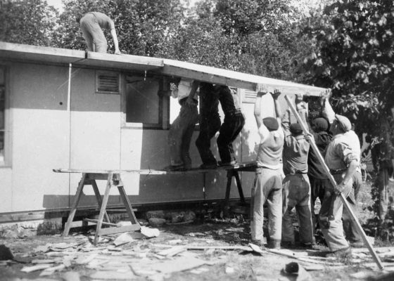 Photographie en noir et blanc représentant un groupe d'hommes en train de monter un bungalow américain de type UK 100 pendant la reconstruction de Saint-Nazaire.