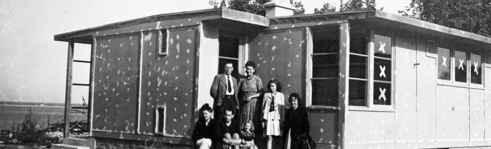 Photographie en noir et blanc d'une famille posant devant un bungalow inachevé,pendant la reconstruction de Saint-Nazaire.