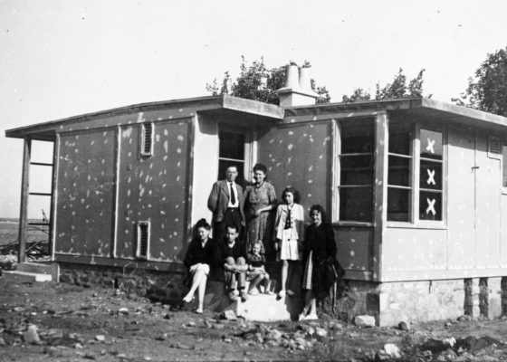 Photographie en noir et blanc d'une famille posant devant un bungalow inachevé,pendant la reconstruction de Saint-Nazaire.