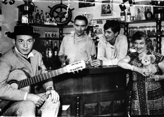 Photographie en noir et blanc représentant des acteurs posant avec le propriétaires du café.