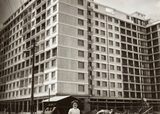 Photographie en noir et blanc représentant une femme posant devant le Building pendant la reconstruction de Saint-Nazaire.