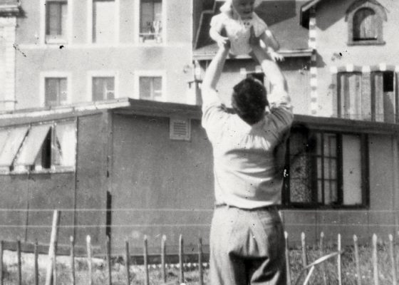 Photographie en noir et blanc représentant un homme portant dans les bras son enfant devant un bungalow pendant la reconstruction à Saint-Nazaire