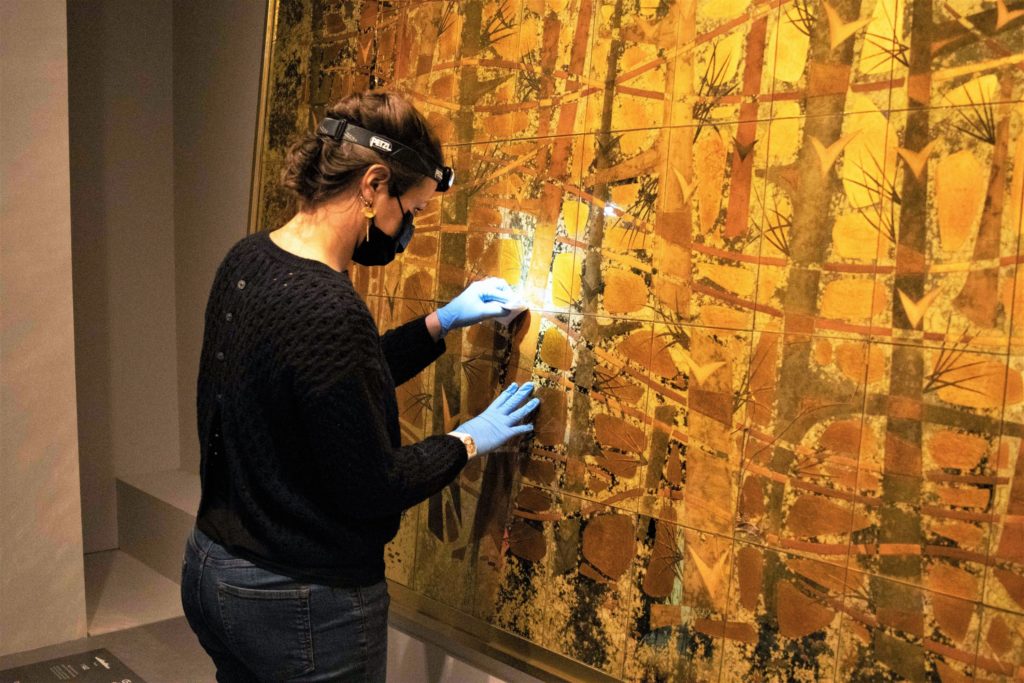 Une professionnelle de musée dépoussière une œuvre en verre églomisé de Pierre et Dominique Lardin provenant du paquebot France (1962).