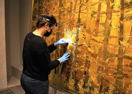 Une professionnelle de musée dépoussière une œuvre en verre églomisé de Pierre et Dominique Lardin provenant du paquebot France (1962).