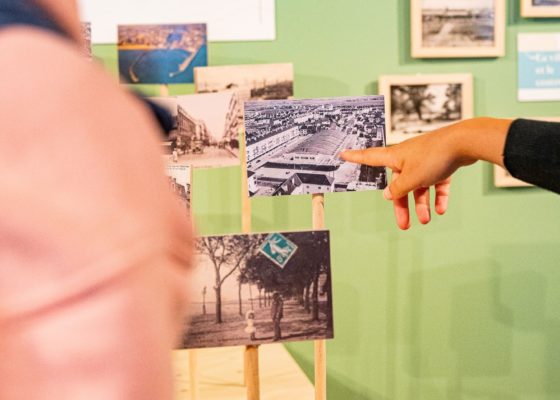 Femme montrant du doigt une carte postale dans l'exposition "Regard miroir ou le paysage réinventé" à l'Écomusée de Saint-Nazaire