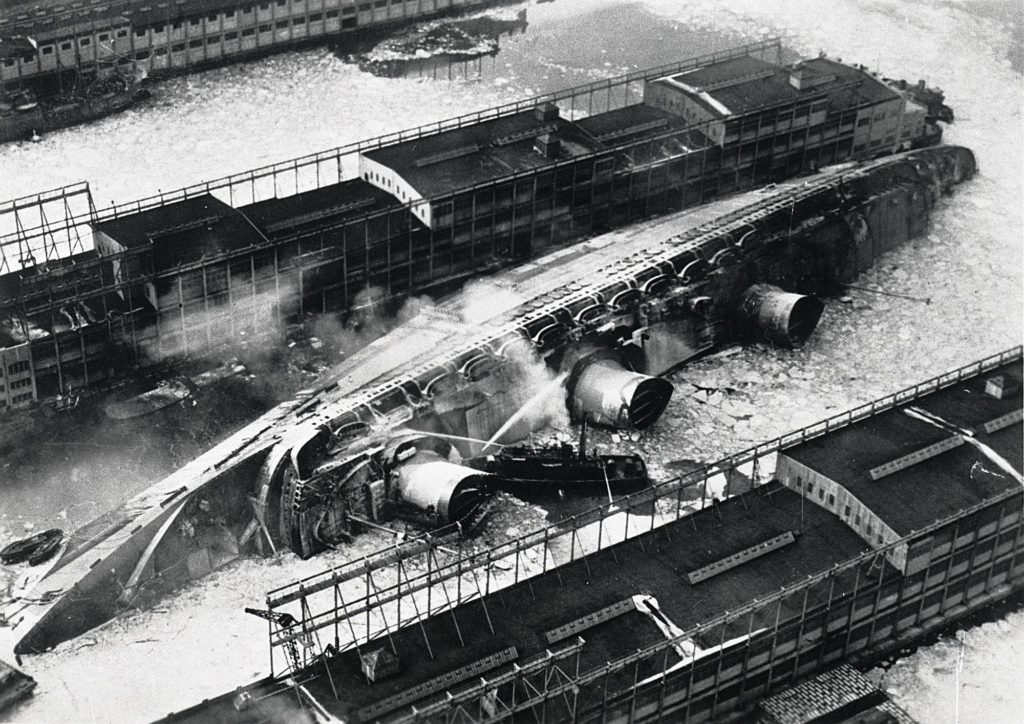 Vue aérienne du paquebot Normandie couché sur son flanc dans le port de New York après son incendie.