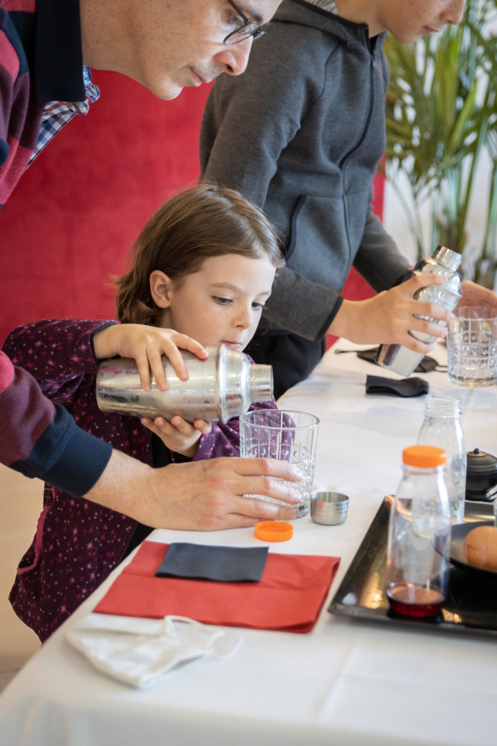 Un père aide sa fille alors qu'elle sert un verre de cocktail avec un shaker lors d'un atelier Cocktail à bord du paquebot France.