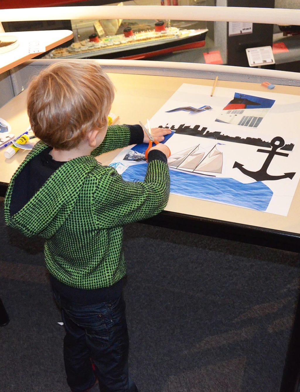 Un petit garçon de dos découpe et colle des images sur une affiche à l'Écomusée lors d'un atelier de la Saison patrimoine.