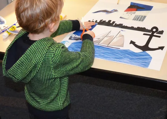 Un petit garçon de dos découpe et colle des images sur une affiche à l'Écomusée lors d'un atelier de la Saison patrimoine.