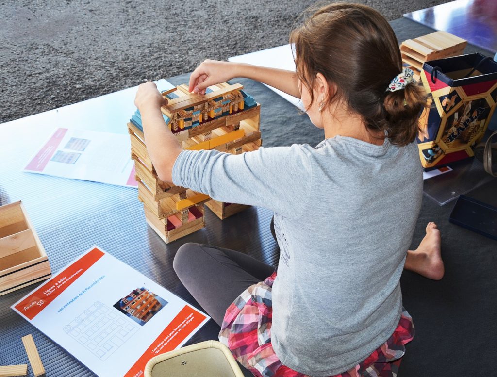 Jeune fille assise par terre en tailleur construisant un bâtiment à partir d'un jeu en bois lors de l'atelier 