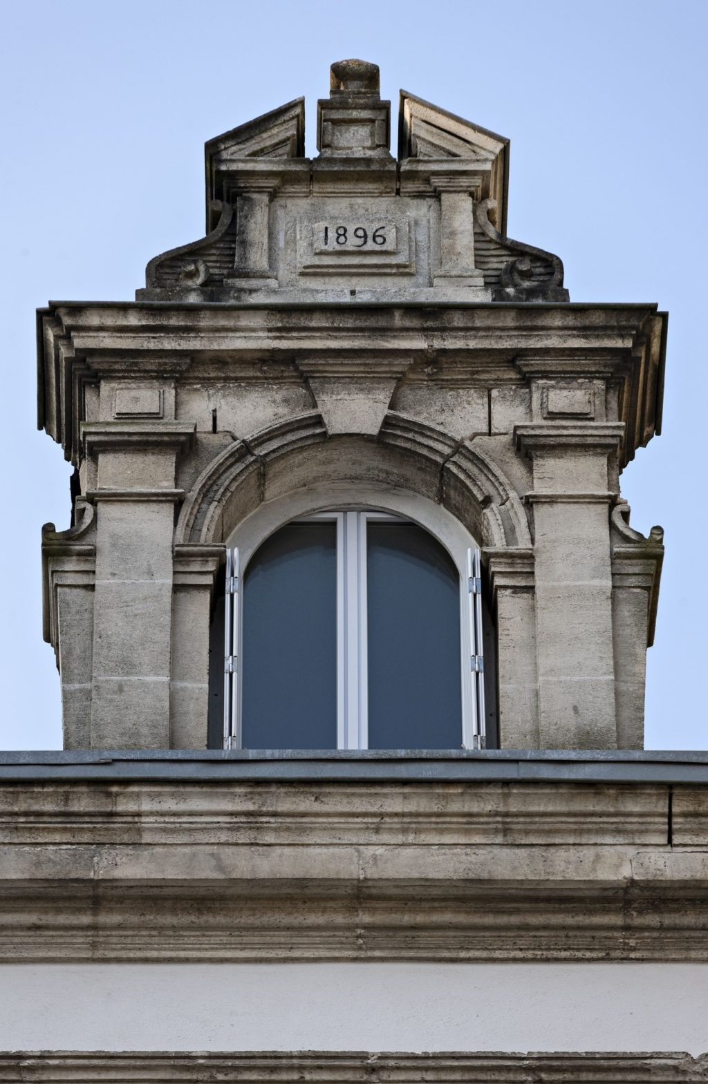 Vue détaillée d'une fenêtre encadrée par deux pilastres. Au-dessus, un fronton avec l'inscription "1896".