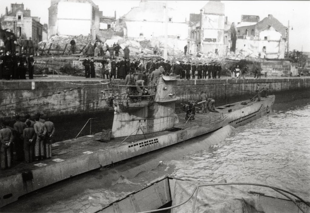 Un sous-marin allemand passe dans l’écluse sud. À l'arrière-plan, les habitations sont en ruine après les bombardements de février 1943.