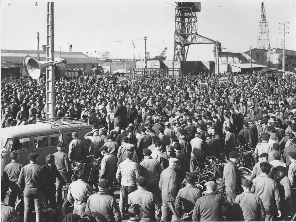 Un homme fait un discours au milieu d'une foule d'ouvriers aux chantiers navals lors des grèves de 1957.