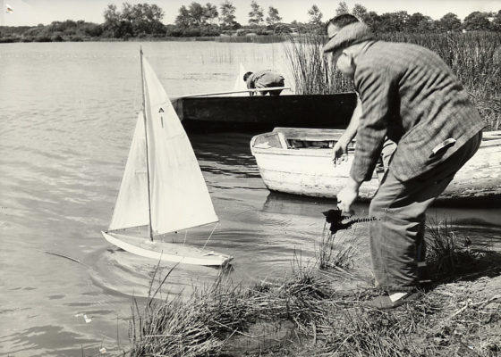 Photographie noir et blanc représentant un vieil homme poussant à l'eau un voilier télécommandé sur l'étang du Bois Joalland.