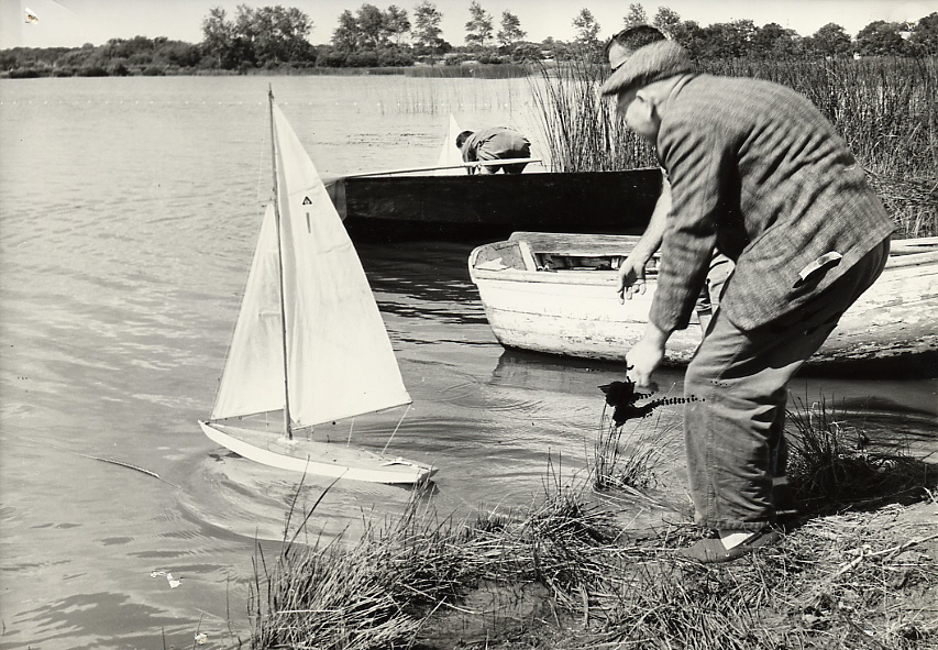 Photographie noir et blanc représentant un vieil homme poussant à l'eau un voilier télécommandé sur l'étang du Bois Joalland.