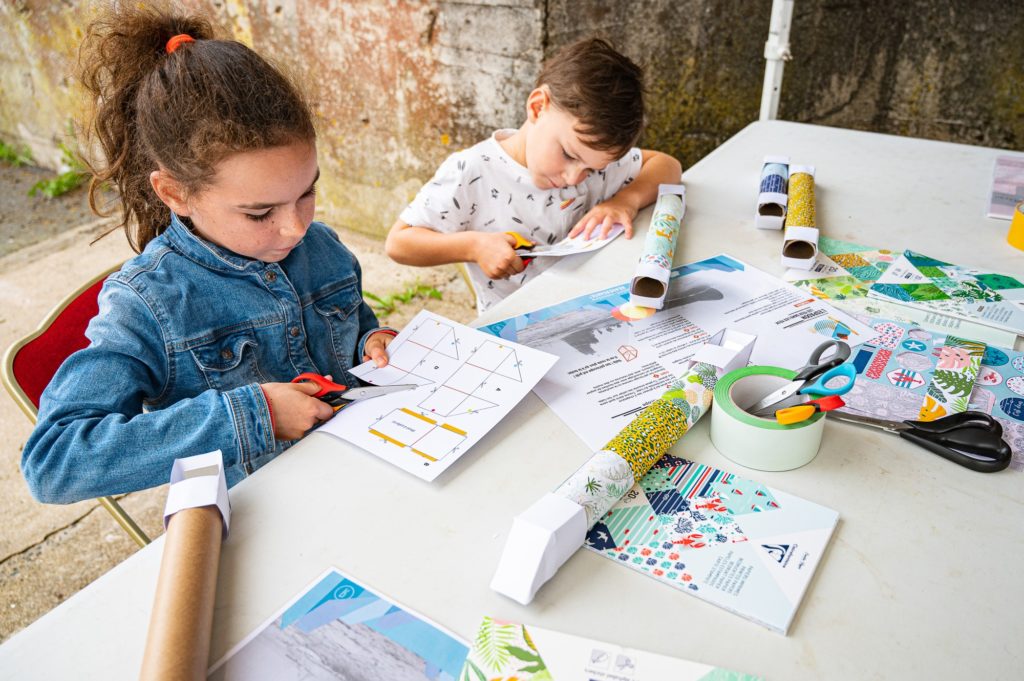 Une petite fille et un petit garçon utilisent des ciseaux lors d'un atelier créatif sur le sous-marin Espadon.