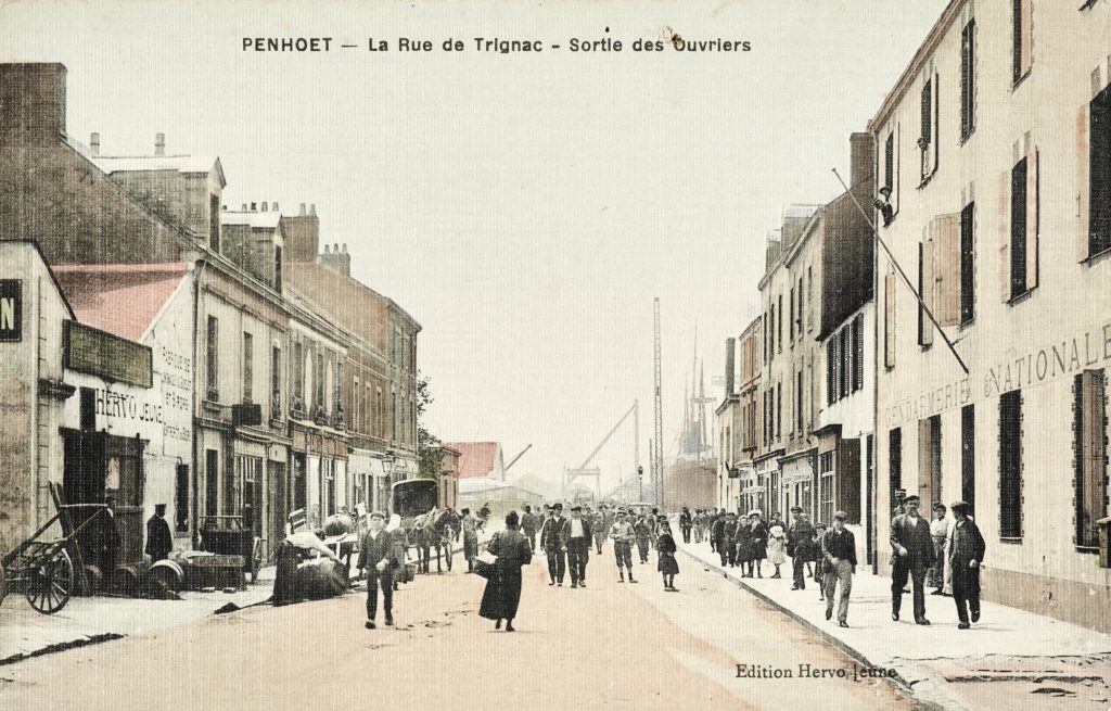 Carte postale colorisée représentant la rue de Trignac très fréquentée lors de la sortie des ouvriers des chantiers dans le quartier de Penhoët.