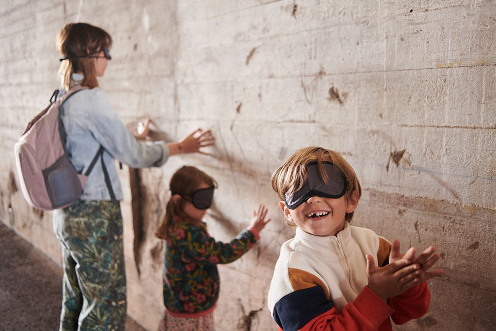 Des visiteurs composés d'une femme et de deux enfants ont les yeux bandés et touchent un mur de la base sous-marine avec leurs mains pendant la visite famille "Sensations béton".