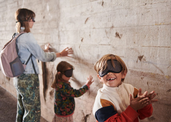 Des visiteurs composés d'une femme et de deux enfants ont les yeux bandés et touchent un mur de la base sous-marine avec leurs mains pendant la visite famille "Sensations béton".