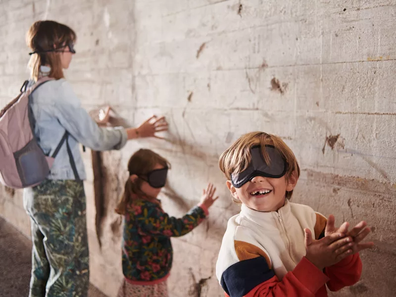 Des visiteurs composés d'une femme et de deux enfants ont les yeux bandés et touchent un mur de la base sous-marine avec leurs mains pendant la visite famille "Sensations béton".
