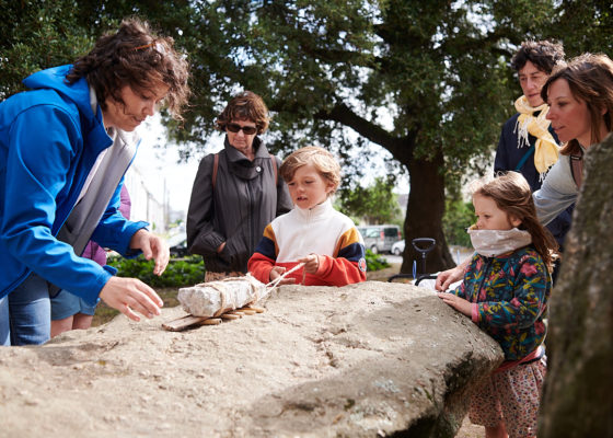 Guide avec des visiteurs adultes et enfants lors d'une visite guidée autour du dolmen de Saint-Nazaire.