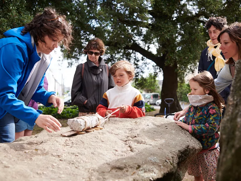 Photographe : Rudy Burbant. Guide avec des visiteurs adultes et enfants lors d'une visite guidée autour du dolmen de Saint-Nazaire.