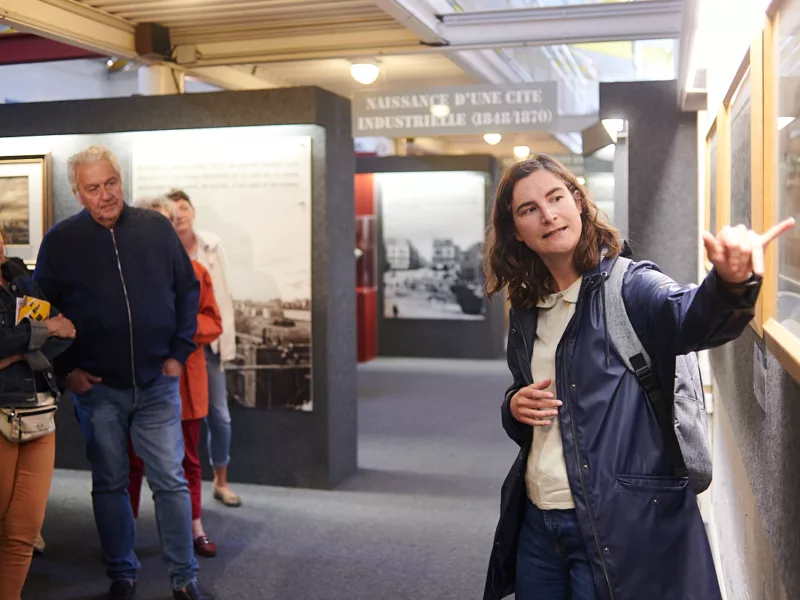 Photographe : Rudy Burbant. Guide montrant une œuvre à un groupe de visiteurs pendant une visite de l'Écomusée.
