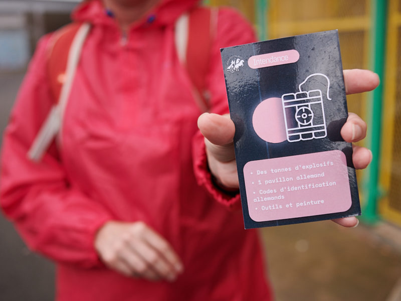 Photographe : Rudy Burbant. Un visiteur montre une carte de jeu pendant la visite participative "Opération Chariot : des commandos dans l'action".