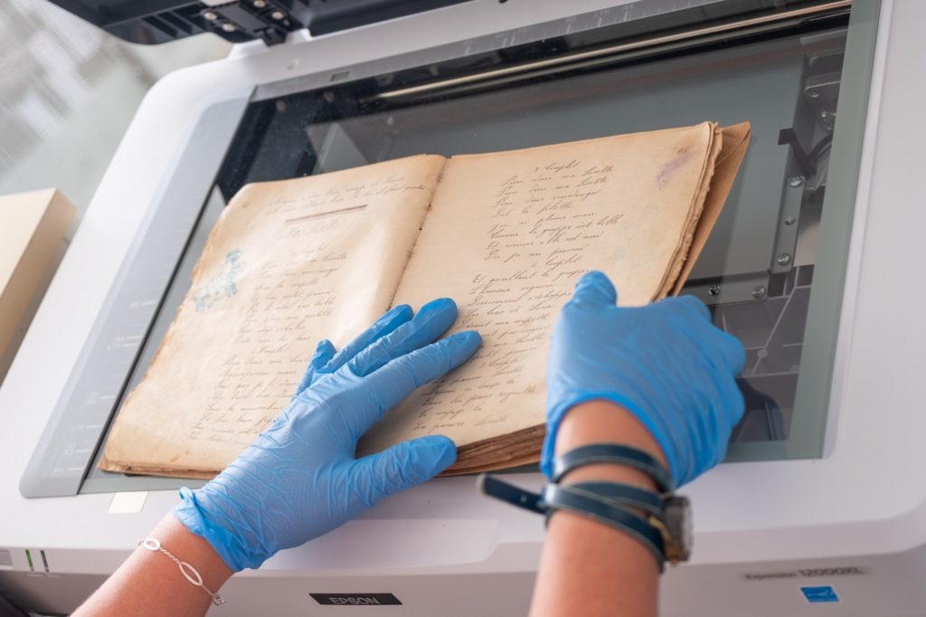 Deux mains gantées numérisent un cahier de chansons datant de la Première Guerre mondiale.